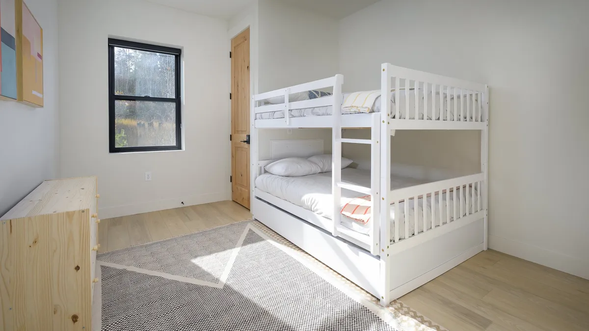 A bright and inviting bunk room with a sturdy bunk bed, a window letting in natural light, and a dresser. The space is perfect for children or families, offering both coziness and a sense of fun.