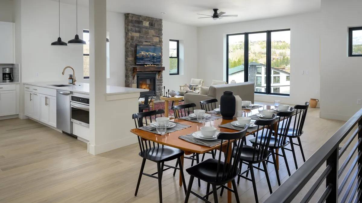 A beautifully set dining table adjacent to a cozy fireplace, large windows offering scenic views, and a glimpse of the modern kitchen appliances in the background. The overall atmosphere is warm, inviting, and perfect for family meals or entertaining guests.