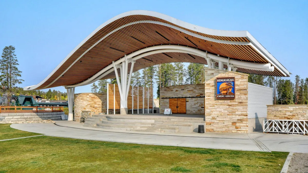 An exterior view of the Hideaway Park amphitheater, characterized by its curved roof structure, stone façade, and a prominent event center sign. The amphitheater is set up for outdoor concerts and community events, making it a recognizable local landmark.