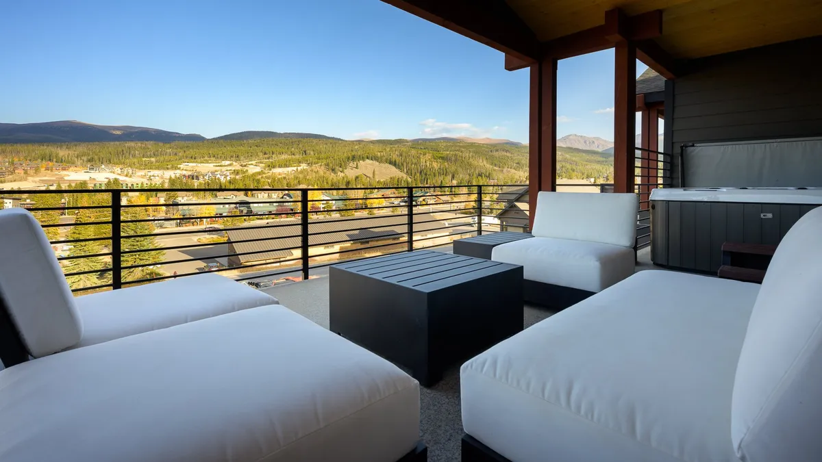 A serene outdoor seating area adjacent to a hot tub, with expansive mountain views in the background. The space is ideal for relaxing, socializing, or enjoying nature at any time of day.