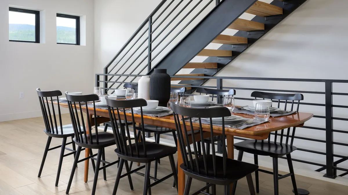 A warm dining area anchored by a large wooden table, surrounded by inviting chairs and a decorative vase. A staircase adds architectural interest, and the open layout connects seamlessly to the living space, reflecting the open-plan design.