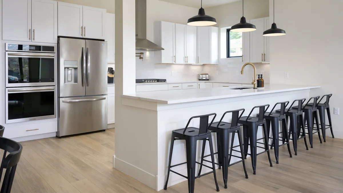 A spacious chef’s kitchen featuring a large kitchen island, sleek stainless steel appliances, modern pendant lighting, and comfortable bar stools. The layout is open and ideal for both meal preparation and casual gatherings, with ample space that encourages social interaction.