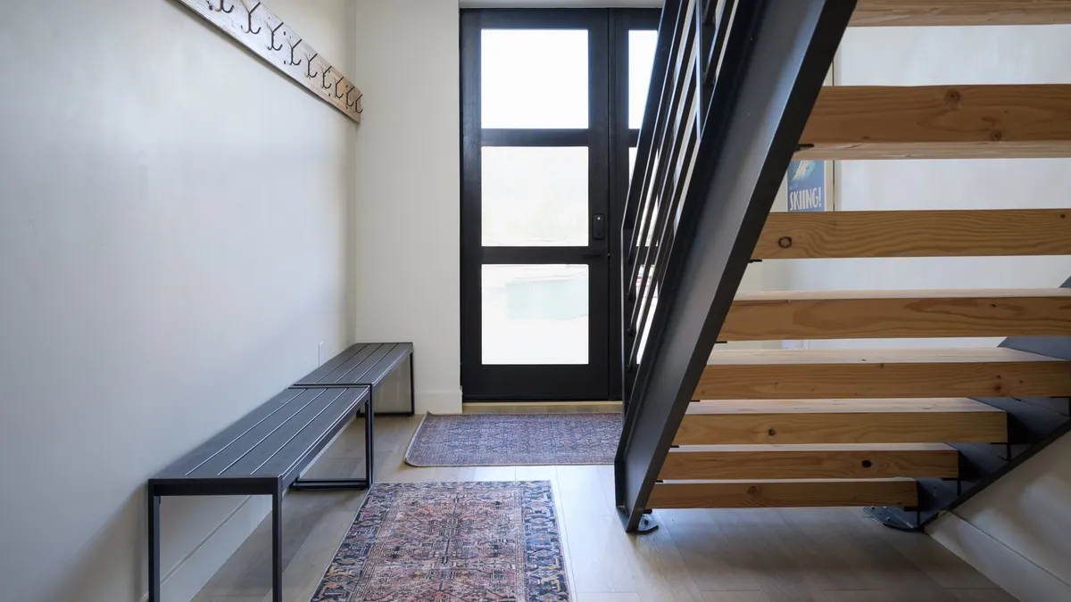 A welcoming interior entryway featuring a staircase, front door, bench, and area rug. This practical space visually connects the interior to the experience of coming and going, hinting at adventure just outside the door.