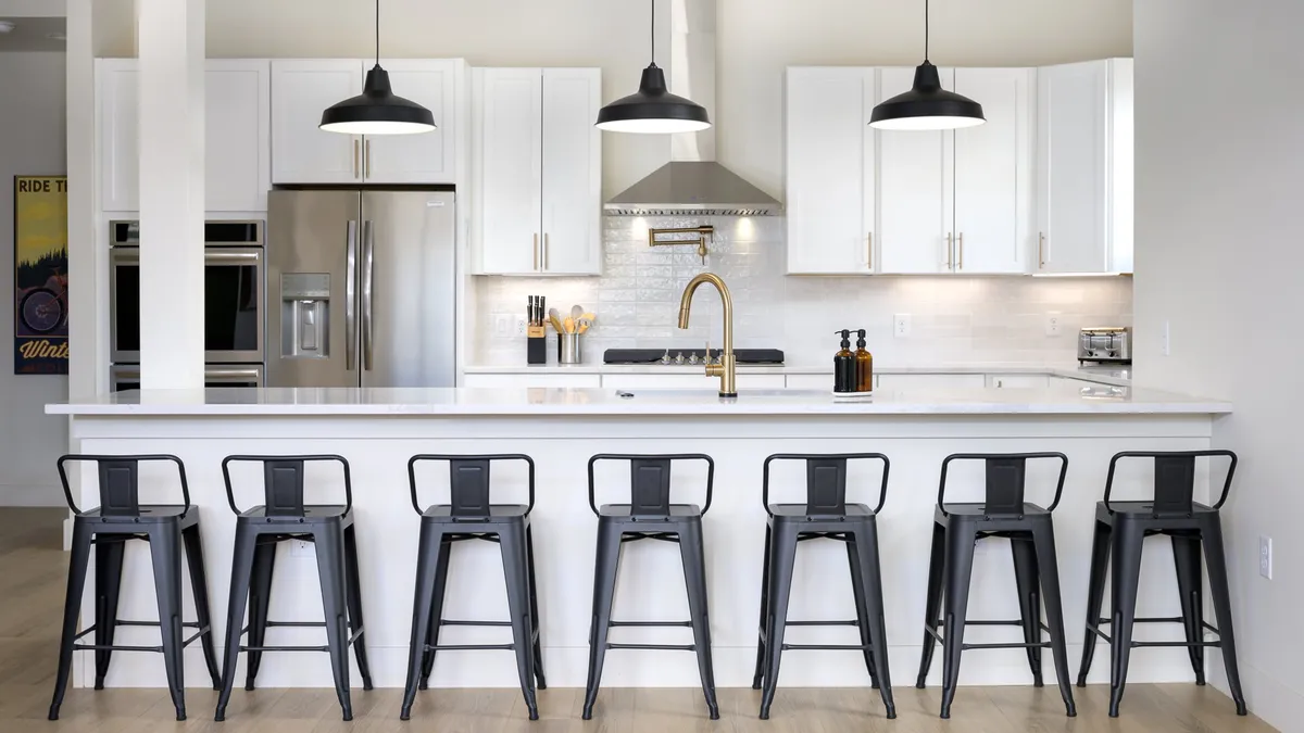 A contemporary kitchen scene with white cabinetry, a stylish golden faucet, pendant lights over a breakfast bar, and bar stools. The space feels bright and inviting, designed for socializing, morning routines, and casual dining.