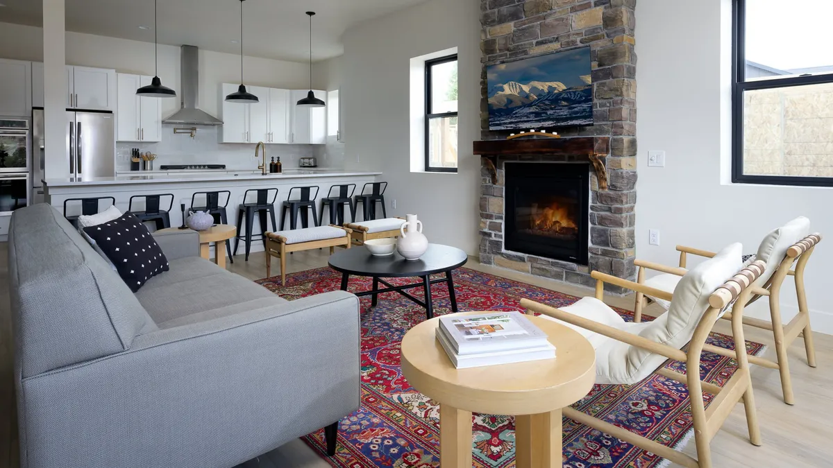 A cozy interior living area with a fireplace, comfortable sofa, kitchen island, and art above the mantel. The space feels inviting and perfect for gathering after outdoor adventures, with a warm ambiance ideal for both relaxation and socializing.