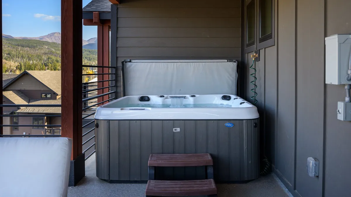 An outdoor hot tub set on a wooden deck with sweeping mountain views. The setting is tranquil, perfect for relaxing soaks after a day of adventure. The image hints at stargazing and sunset experiences from the tub.