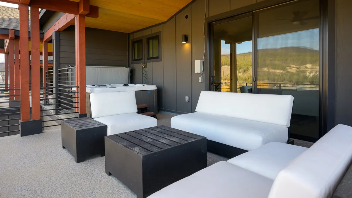 An inviting outdoor patio area featuring plush white sofas, a sleek black coffee table, and a bubbling hot tub—all set against an open sky. The space is ideal for family gatherings, relaxation, and enjoying fresh air together.